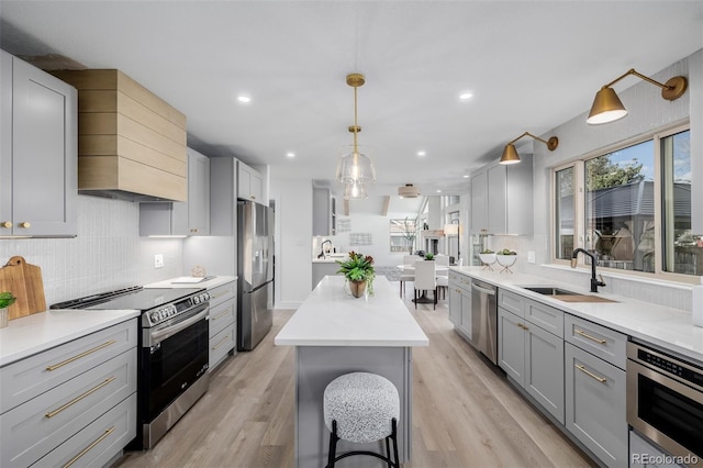 kitchen with pendant lighting, sink, gray cabinetry, stainless steel appliances, and a kitchen island