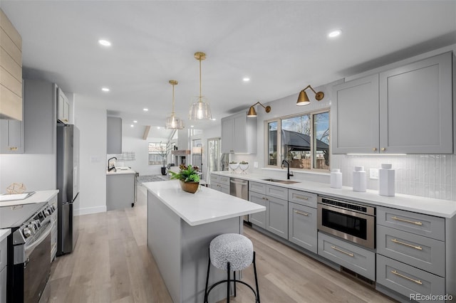 kitchen featuring sink, gray cabinetry, stainless steel appliances, a center island, and decorative light fixtures