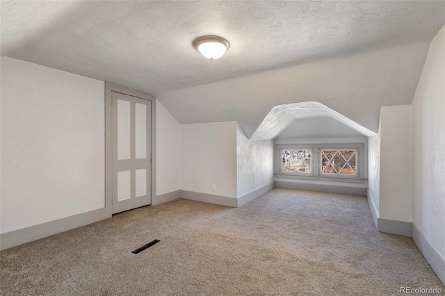 bonus room featuring vaulted ceiling, light colored carpet, and a textured ceiling