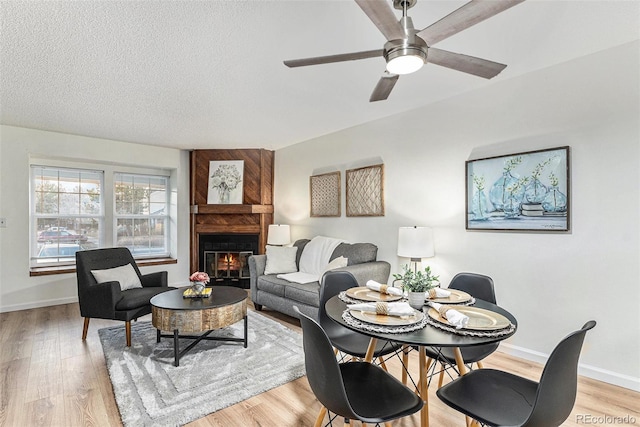 dining room featuring a large fireplace, ceiling fan, light hardwood / wood-style flooring, and a textured ceiling