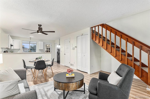 living room featuring ceiling fan, light hardwood / wood-style floors, and a textured ceiling