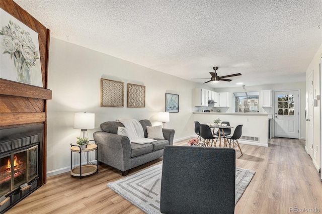 living room with ceiling fan, light hardwood / wood-style floors, and a textured ceiling