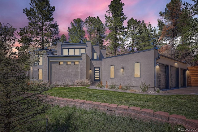 modern home with a garage, driveway, a front yard, and stucco siding