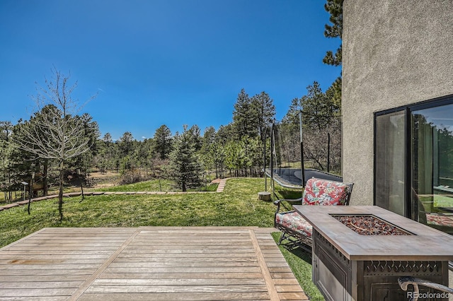 wooden deck with a trampoline, an outdoor fire pit, and a yard