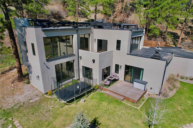 back of property with a lawn, a deck, a balcony, and stucco siding