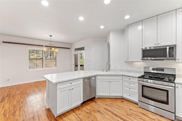 kitchen with appliances with stainless steel finishes, kitchen peninsula, light wood-type flooring, and sink