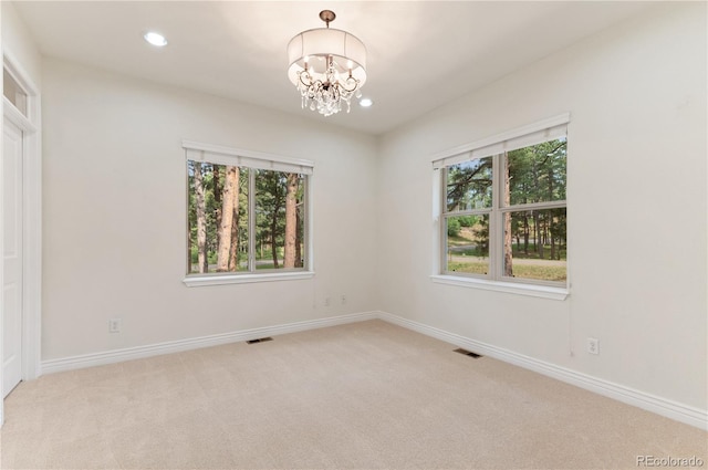 spare room with a notable chandelier, plenty of natural light, and light colored carpet