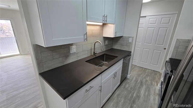 kitchen with light wood-type flooring, stainless steel appliances, a sink, dark countertops, and tasteful backsplash