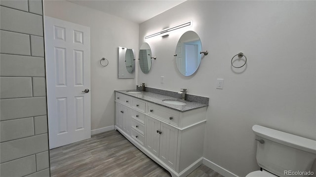 bathroom with toilet, wood finished floors, baseboards, and a sink