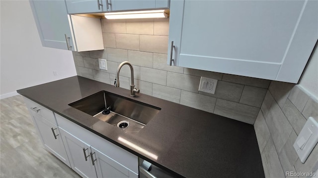 kitchen featuring a sink, white cabinets, dark countertops, tasteful backsplash, and light wood-type flooring