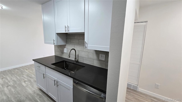 kitchen with a sink, decorative backsplash, light wood-style floors, stainless steel dishwasher, and dark countertops