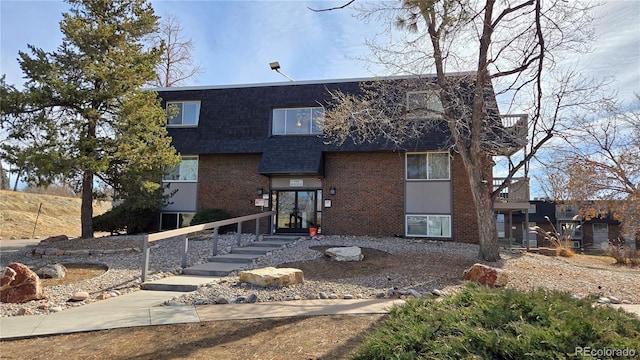 view of front of home featuring brick siding, mansard roof, and a shingled roof