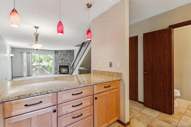 kitchen featuring light stone counters, a textured ceiling, a stone fireplace, and pendant lighting