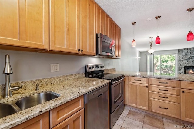 kitchen with light stone countertops, decorative light fixtures, a stone fireplace, appliances with stainless steel finishes, and a sink