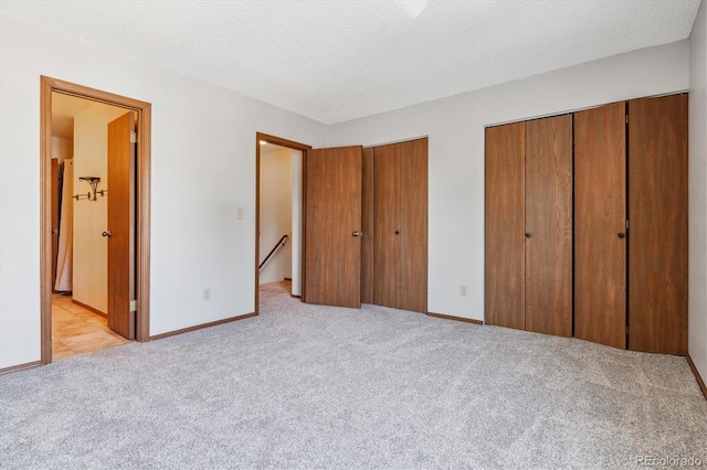 unfurnished bedroom featuring baseboards, ensuite bath, a textured ceiling, light colored carpet, and two closets