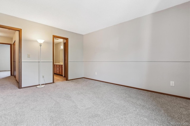 unfurnished bedroom featuring baseboards, light colored carpet, and ensuite bath