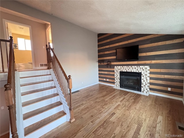 unfurnished living room with wood-type flooring, a textured ceiling, vaulted ceiling, and a tiled fireplace