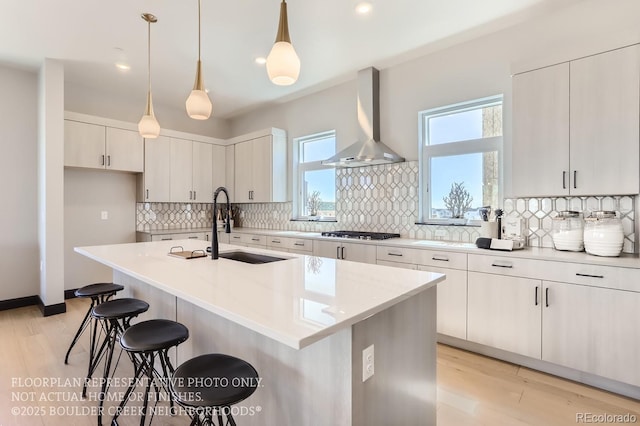 1768 Peak Loop, Broomfield, CO 80023 - kitchen featuring wall chimney range hood, stainless steel gas stovetop, a breakfast bar, decorative backsplash, and light wood-type flooring