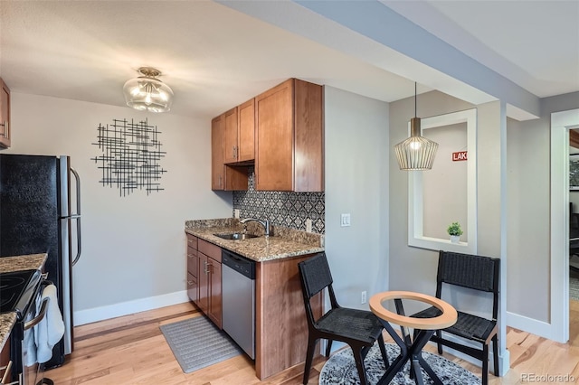 kitchen with light stone counters, backsplash, appliances with stainless steel finishes, brown cabinetry, and light wood-type flooring