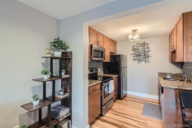 2460 W Caithness Pl Unit 104, Denver, CO 80211 - kitchen featuring stainless steel appliances, light wood finished floors, tasteful backsplash, light stone counters, and brown cabinetry