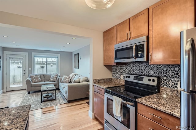 kitchen with dark stone counters, decorative backsplash, brown cabinetry, stainless steel appliances, and light wood-style floors