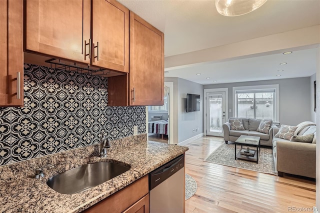 kitchen featuring light stone counters, tasteful backsplash, light wood-style flooring, a sink, and dishwasher