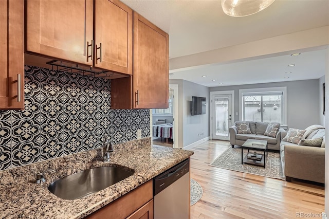 2460 W Caithness Pl Unit 104, Denver, CO 80211 - kitchen featuring stainless steel dishwasher, light wood-style floors, light stone countertops, open floor plan, and brown cabinetry