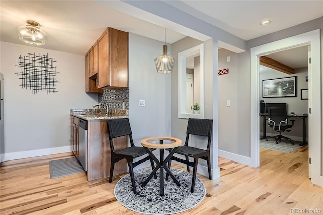 kitchen with baseboards, light wood-type flooring, backsplash, dishwasher, and brown cabinetry