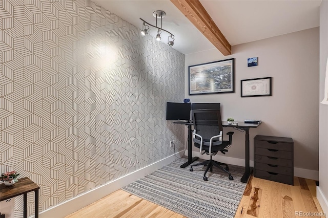 office space with an accent wall, beam ceiling, baseboards, and wood finished floors