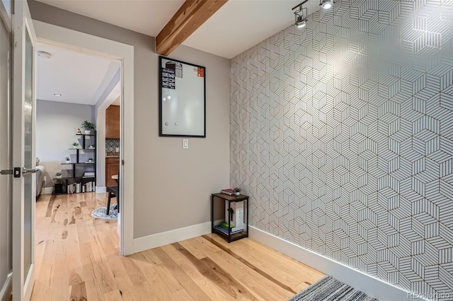 hall featuring light wood finished floors, baseboards, and beam ceiling