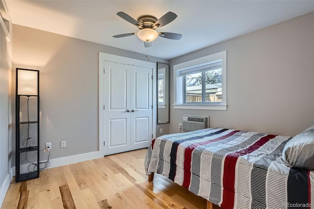 bedroom featuring ceiling fan, baseboards, light wood-style floors, an AC wall unit, and a closet