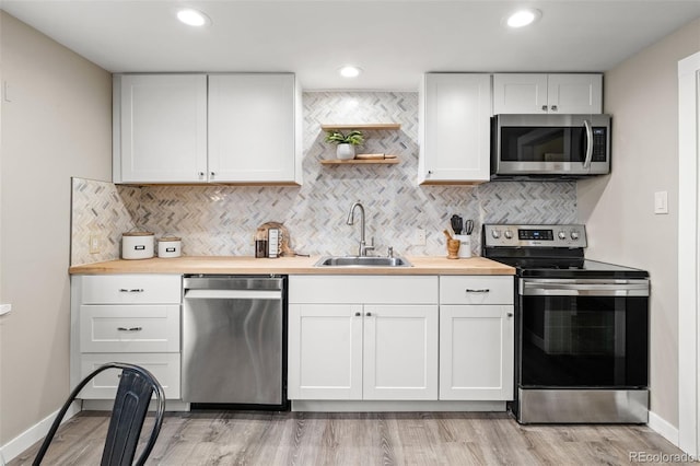 kitchen with stainless steel appliances, wooden counters, sink, and white cabinets