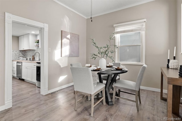 dining area featuring crown molding, sink, and light hardwood / wood-style flooring