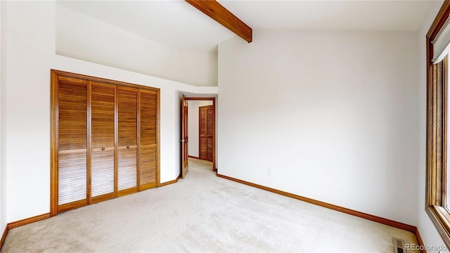 unfurnished bedroom with light carpet, a closet, and lofted ceiling with beams