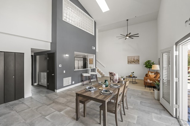 living area featuring ceiling fan, a skylight, visible vents, baseboards, and stairs