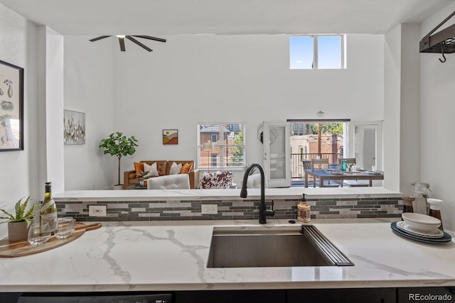 kitchen with a towering ceiling, light stone counters, open floor plan, a sink, and backsplash