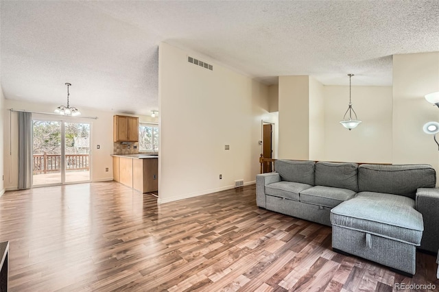 living area with light wood finished floors, a textured ceiling, visible vents, and a notable chandelier