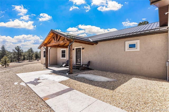 rear view of house with a patio area, stucco siding, and metal roof