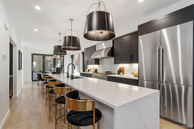 3709 Tejon St, Denver, CO 80211 - kitchen with appliances with stainless steel finishes, wall chimney range hood, recessed lighting, an island with sink, and light wood finished floors