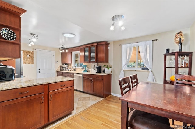 kitchen featuring light stone counters, backsplash, stainless steel dishwasher, and light hardwood / wood-style floors