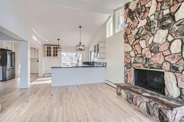 kitchen featuring a stone fireplace, stainless steel fridge, decorative light fixtures, white cabinetry, and kitchen peninsula