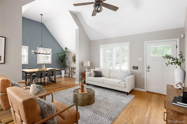 living area with ceiling fan with notable chandelier, light wood-type flooring, lofted ceiling, and baseboards