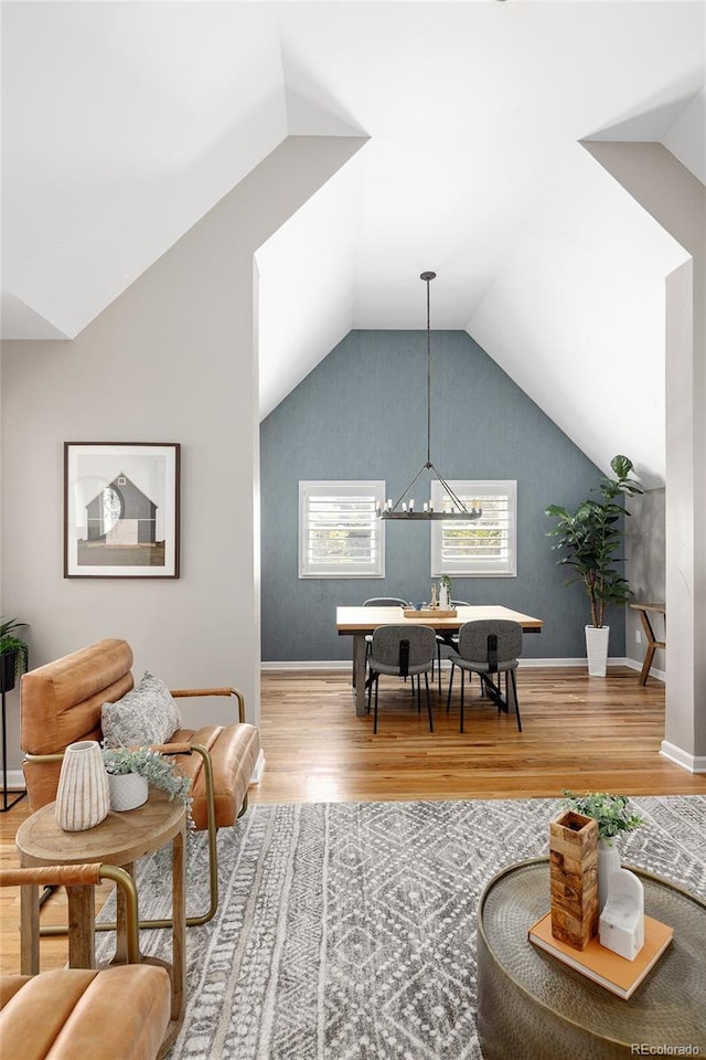 living room featuring a notable chandelier, baseboards, lofted ceiling, and wood finished floors