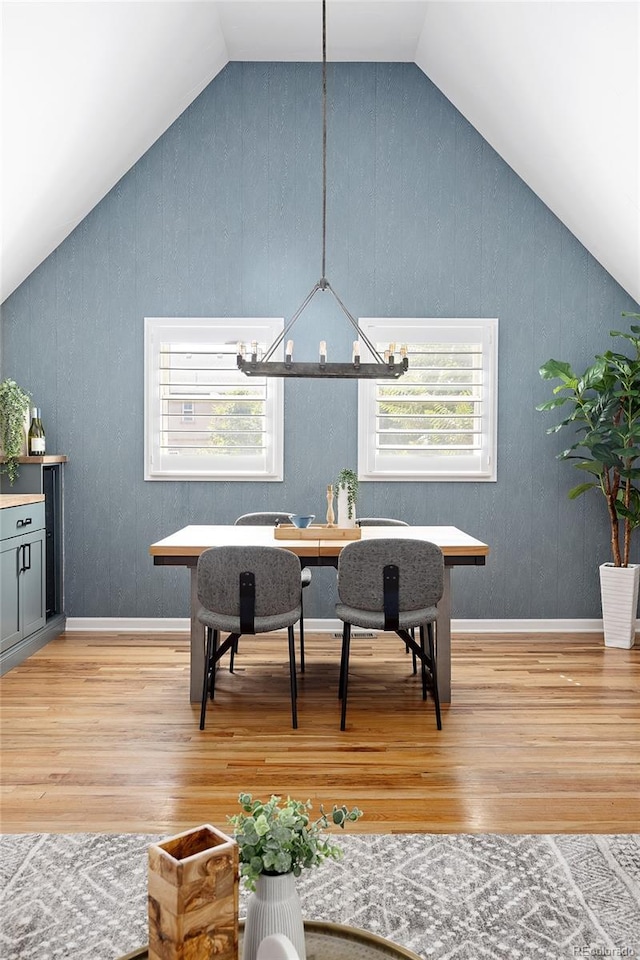 dining area with baseboards, lofted ceiling, a notable chandelier, and light wood-type flooring
