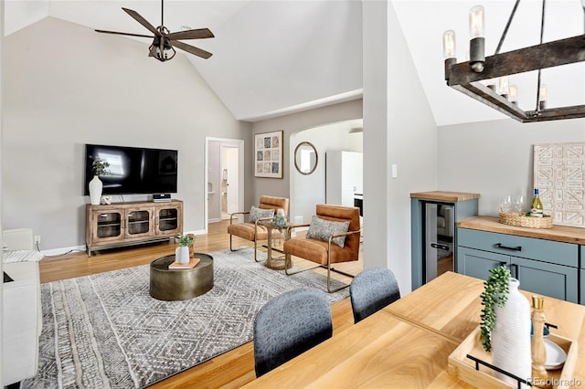 living room featuring wood finished floors, a ceiling fan, arched walkways, a dry bar, and beverage cooler