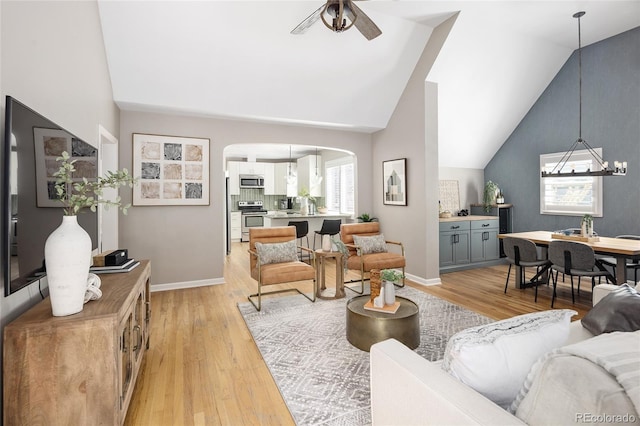 living room with light wood-type flooring, lofted ceiling, baseboards, ceiling fan with notable chandelier, and arched walkways