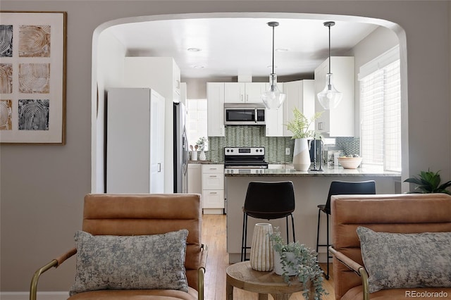 kitchen featuring white cabinetry, decorative backsplash, arched walkways, a peninsula, and appliances with stainless steel finishes