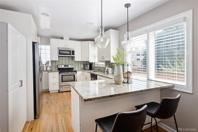 kitchen featuring a peninsula, appliances with stainless steel finishes, a sink, light stone counters, and backsplash