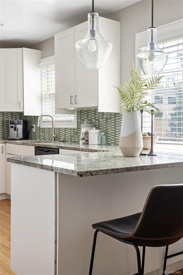 kitchen with a breakfast bar, white cabinetry, light wood-style flooring, and backsplash
