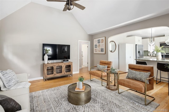 living room with light wood-style flooring, high vaulted ceiling, baseboards, arched walkways, and a ceiling fan